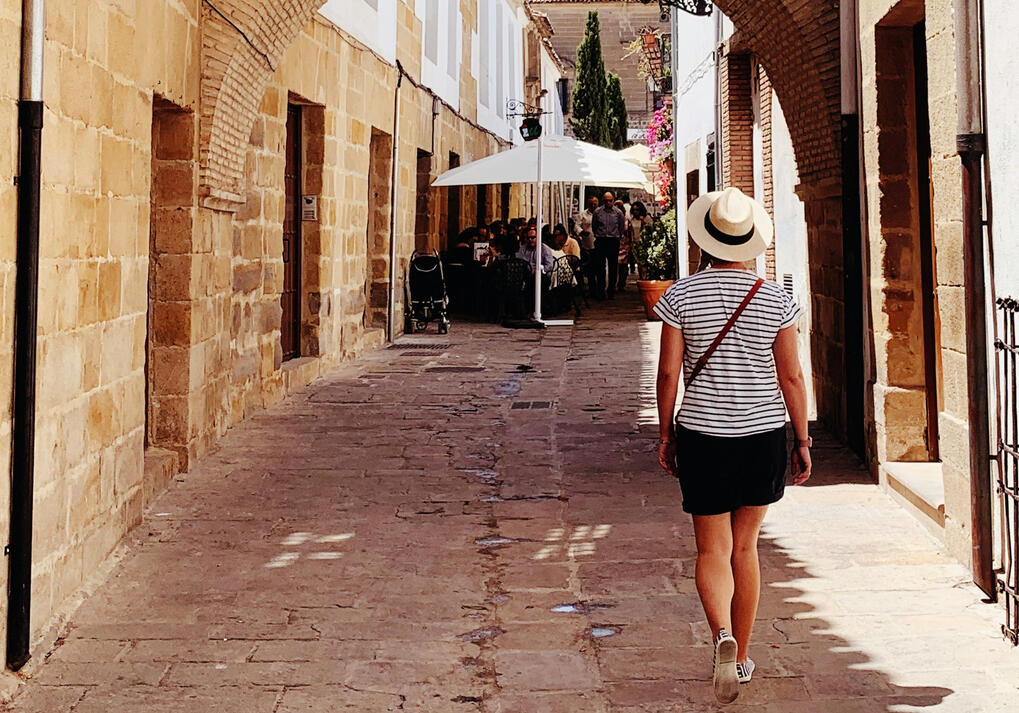 Woman walking through a sunlit stone alleyway in Spain