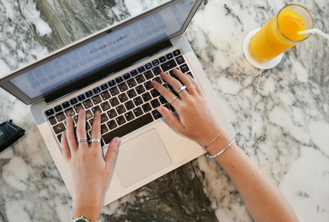 Hands typing on a laptop beside a glass of orange juice
