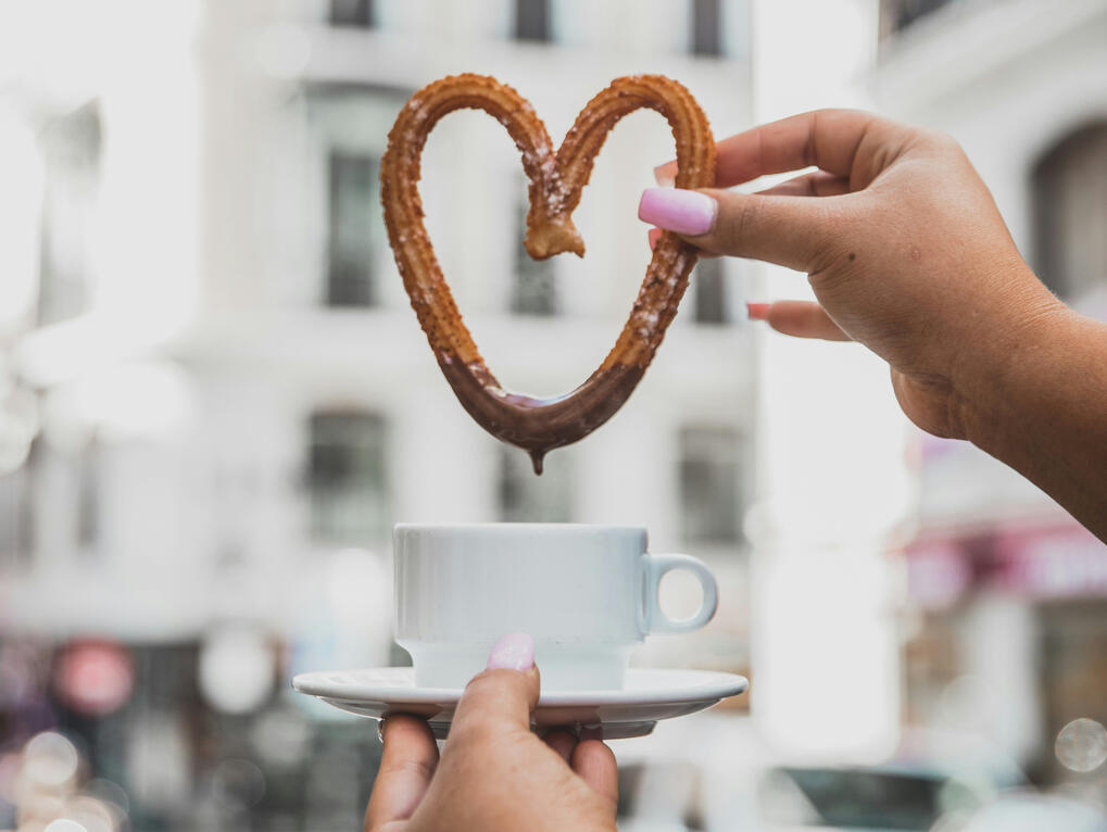 Heart-shaped churro held above a cup of coffee